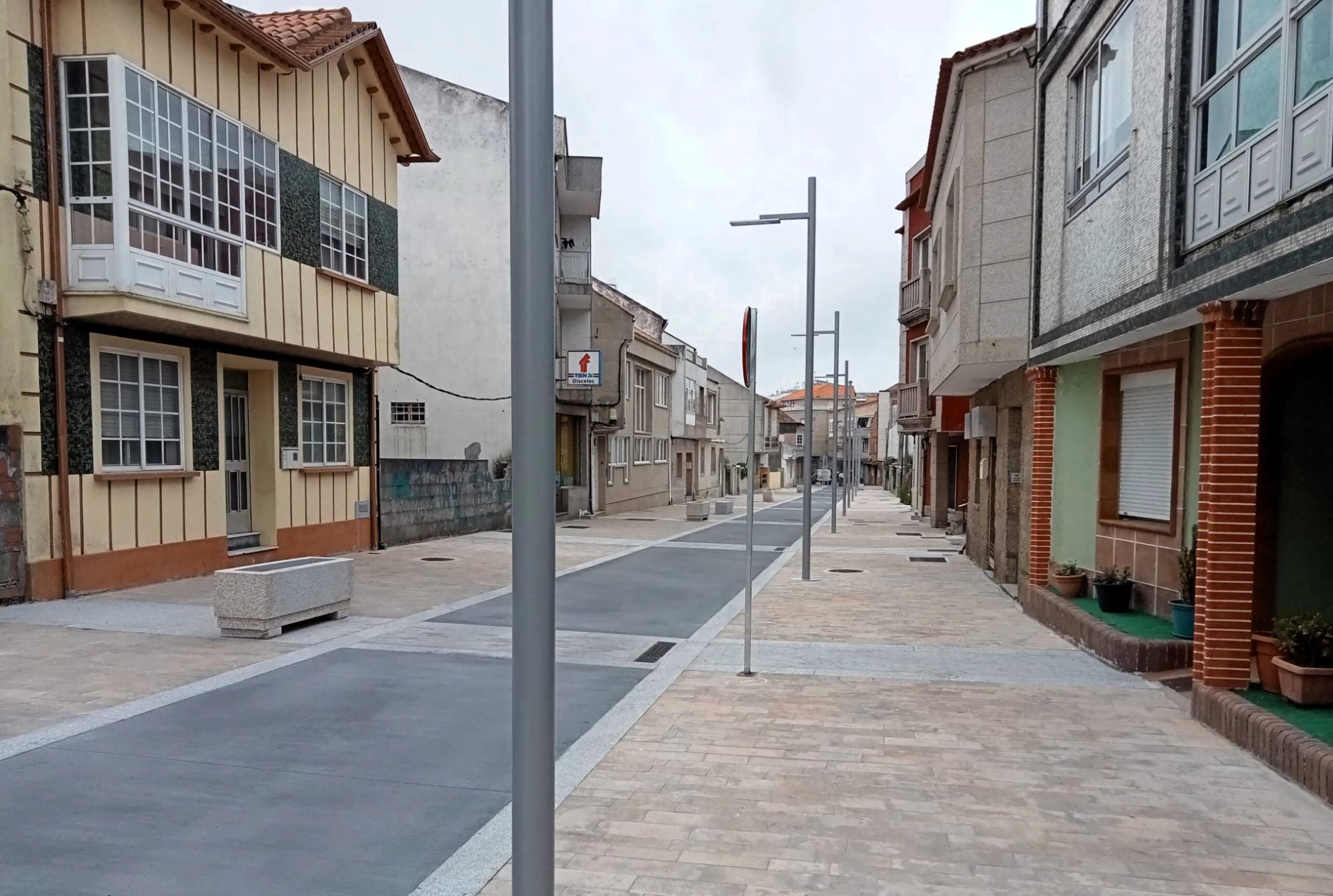 Avenida de Castelao en Illa de Arousa. Las aceras y la calzada forman plataforma continua delimitada por cambios en el pavimento. Con bancos, jardineras y farolas añadidos tras la remodelación.
