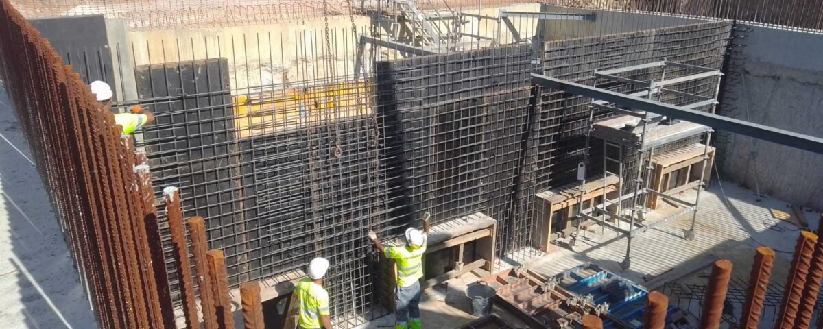 Dos trabajadores en una obra con una estructura de acero rodeada de hormigón