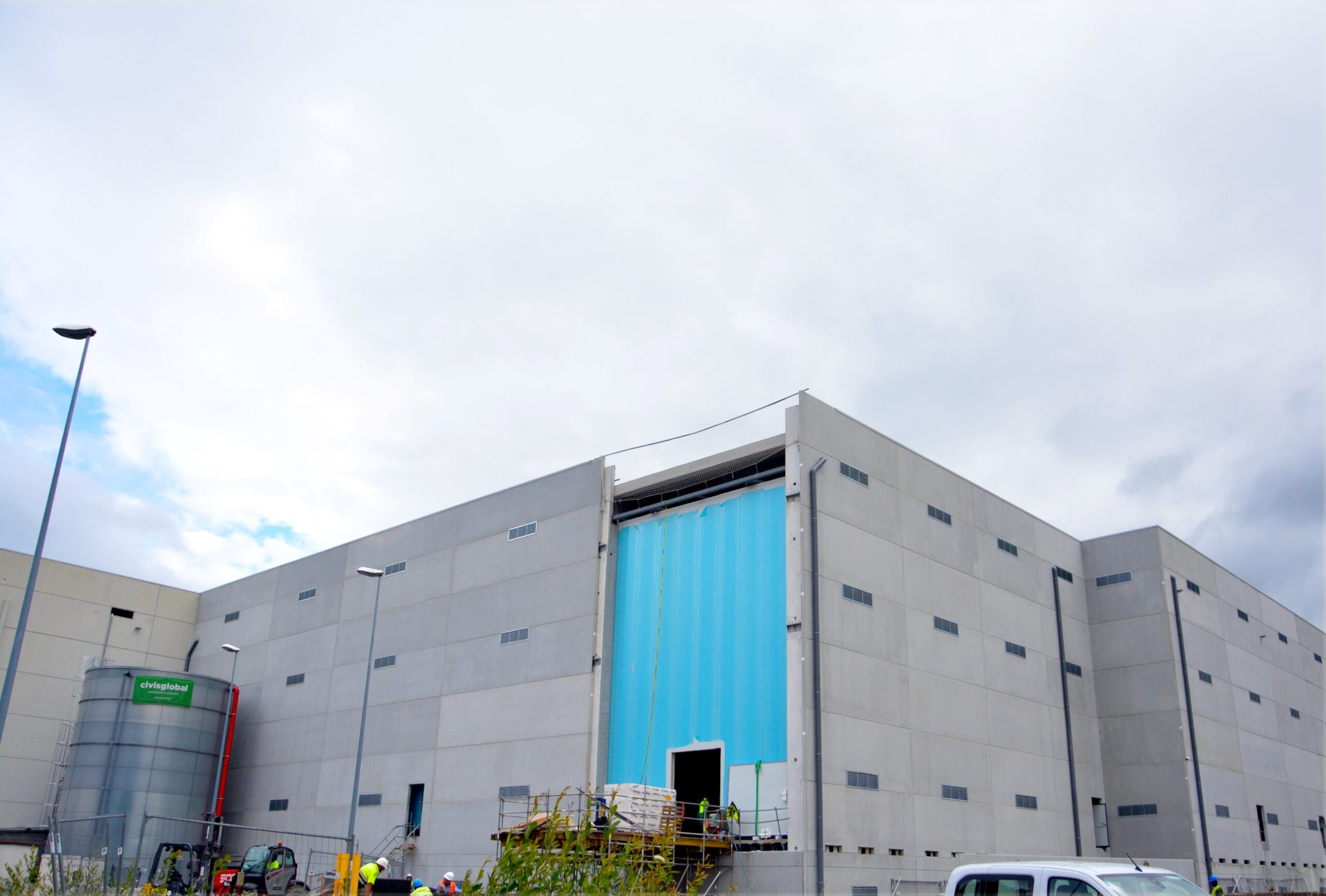 Vista exterior de una nave industrial con una gran puerta de acceso en construcción y un depósito metálico adosado a la fachada