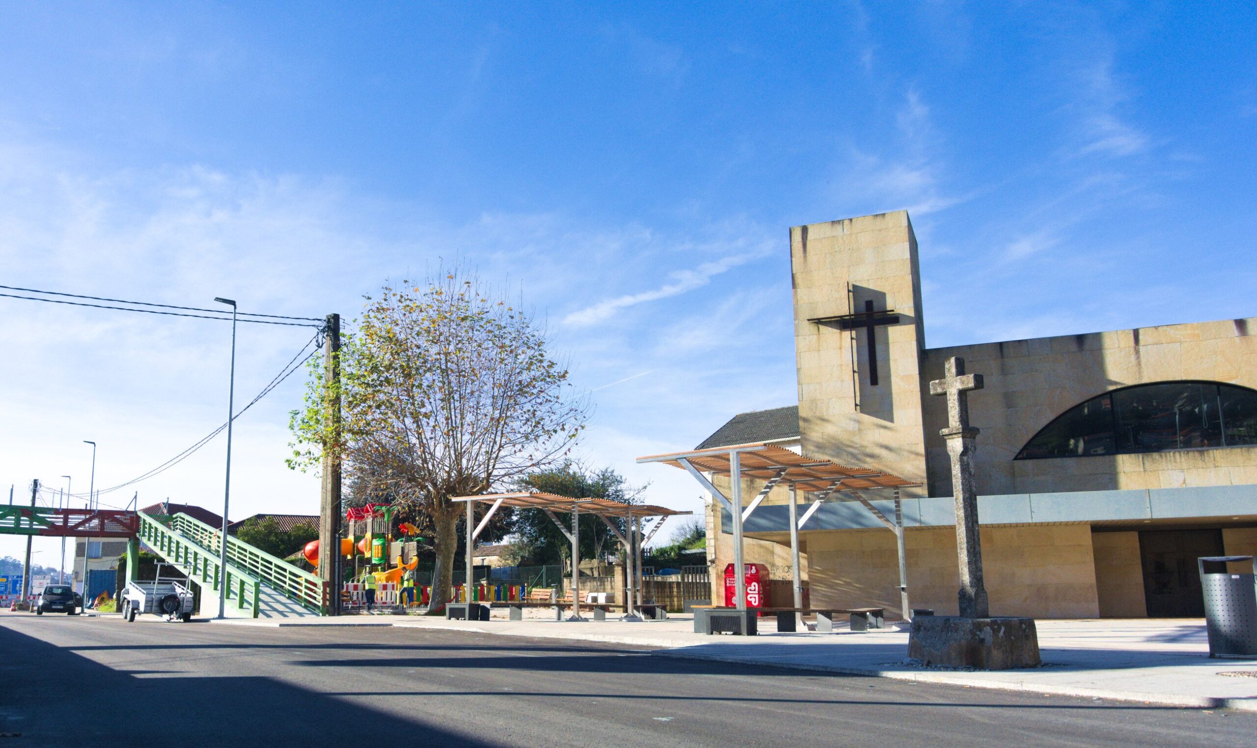 zona de plaza frente a una iglesia, con una pasarela peatonal junto a un parque infantil