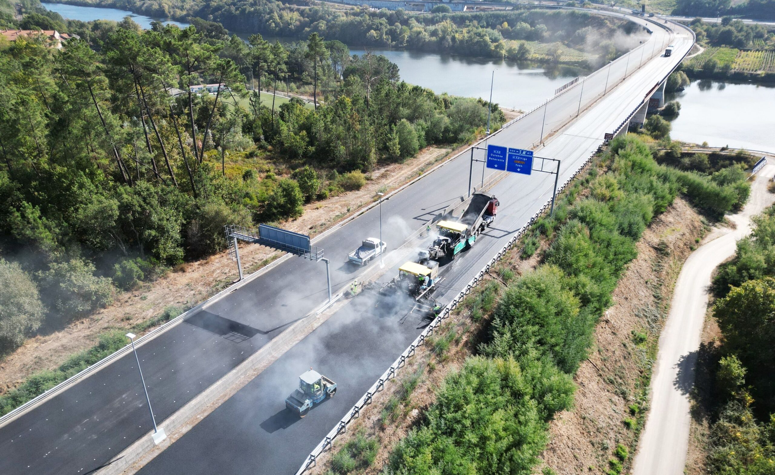 autovía con dos carriles con maquinaria trabajando en la calzada. Al fondo un viaducto sobre el río